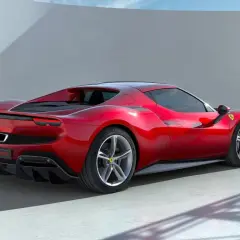 Czerwone Ferrari 296 GTB widziane z tyłu, na tle białej ściany i nieba.