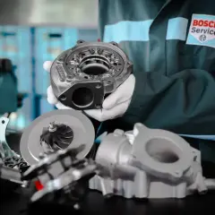 Mechanik w fartuchu Bosch Service prezentuje części turbosprężarki, pokazując jak sprawdzić turbinę.
