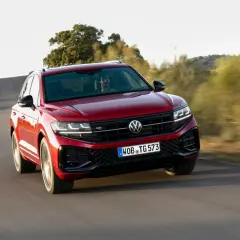 Czerwony Volkswagen Touareg 2024 pędzi po krętej drodze wśród wzgórz.