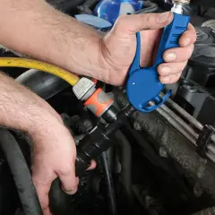 Ręce mechanika podłączają niebieskie narzędzie do węża, przygotowując środek do płukania układu chłodzenia.