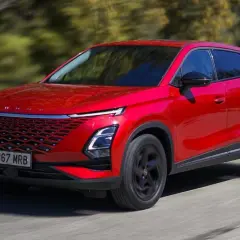 Czerwony, nowoczesny SUV, jeden z chińskich samochodów elektrycznych, jedzie po drodze wśród drzew.
