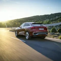 Czerwony samochód Audi coupe na krętej drodze w górach o zachodzie słońca.