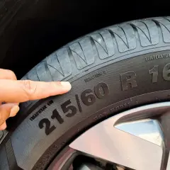 Palec wskazuje na oznaczenie opon 215/60 R16, informujące o rozmiarze i typie.