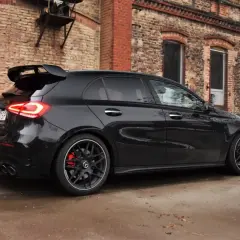 Czarny Mercedes-AMG A45s z dużym spojlerem i czerwonymi zaciskami hamulcowymi stoi przed starą ceglaną kamienicą.