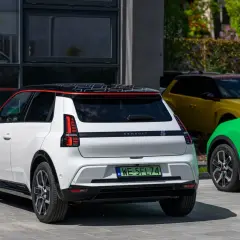 Biały Renault 5 E-Tech elektryczny z czarnym dachem i czerwonymi akcentami, obok zielonego i żółtego samochodu.