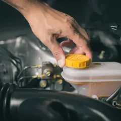 Dłoń odkręca żółtą zakrętkę zbiornika płynu hamulcowego. To właśnie tam znajduje się zbiornik płynu hamulcowego BMW E39.