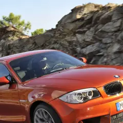 Pomarańczowy bmw1 z kierowcą za kierownicą pędzi po górskiej drodze.