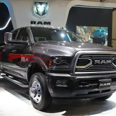Ciemnoszary Dodge Ram 3500 z podwójnymi tylnymi kołami prezentuje się na wystawie, obok białego pickupa.
