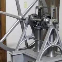 Mechanizm z kołem zamachowym i zębatkami, przypominający wczesne próby stworzenia silnika spalinowego.
