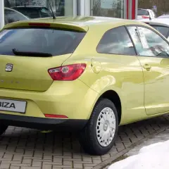 Jasnożółty Seat Ibiza 1.4 benzyna z tyłu, zaparkowany na kostce brukowej, obok śniegu.