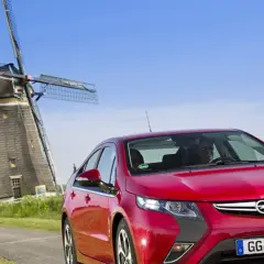 Czerwony Opel Ampera na tle wiatraków w Holandii.