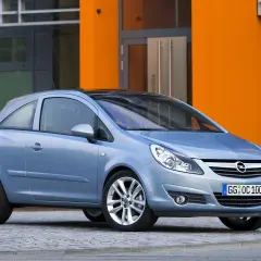 Niebieski Opel Corsa D 1.2 benzyna stoi przed pomarańczowym budynkiem.