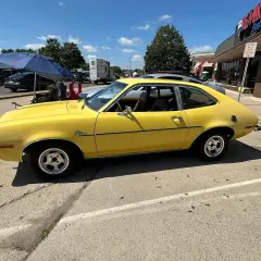 Żółty Ford Pinto z lat 70. stoi zaparkowany przy ulicy, obok sklepu.