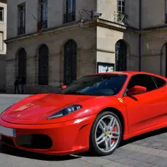 Czerwone Ferrari F430 zaparkowane na brukowanej ulicy przed kamienną kamienicą.