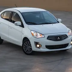 Biały sedan Mitsubishi Mirage zaparkowany na betonowej nawierzchni.
