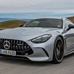 Srebrny Mercedes-AMG GT sunie po krętej drodze, ukazując swoją sportową sylwetkę i potężny grill.