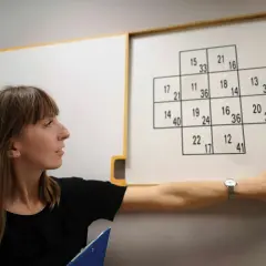 Kobieta wskazuje na tablicę z zadaniem liczbowym, przypominającym test psychologiczny.