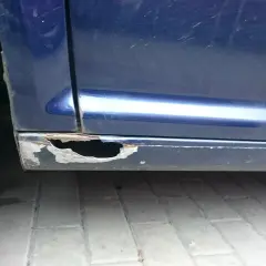 Widoczne są poważne dziury w progach niebieskiego samochodu, co pokazuje, jak załatać dziury w samochodzie.