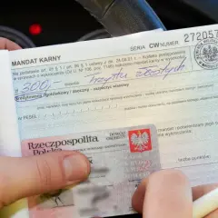 Mandat karny na 300 zł za wykroczenie. W tle widać fragment deski rozdzielczej samochodu, sugerujący, że zdarzenie miało miejsce na skrzyżowaniu.