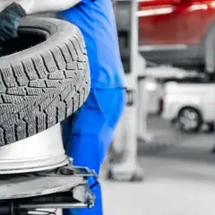Mechanik w niebieskim kombinezonie wymienia oponę. Dowiedz się, ile kosztuje wymiana opon w Twojej okolicy.
