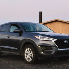 Ciemnoszary Hyundai Tucson zaparkowany przy drewnianej budowli. Zastanawiasz się, ile pali ten model?