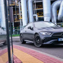 Ciemnoszary Mercedes-Benz CLE Coupé na tle przemysłowych rur i budynków.