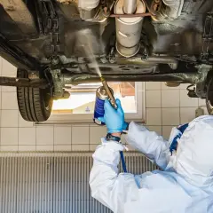 Mechanik w kombinezonie ochronnym zabezpiecza podwozie auta. Zastanawiasz się, ile kosztuje przegląd samochodu z gazem?