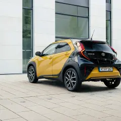 Żółto-czarny crossover Toyota Aygo X stoi na placu przed nowoczesnym budynkiem.