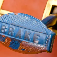 Niebieska, wytarta dźwignia z napisem "BRAKE" i ślady rdzy. Może potrzebuje smaru do prowadnic hamulcowych, by znów działać płynnie.