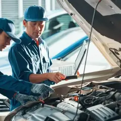 Mechanicy sprawdzają silnik samochodu, analizując dane na laptopie. Planują zastosowanie ceramizera do silnika, by poprawić jego pracę.
