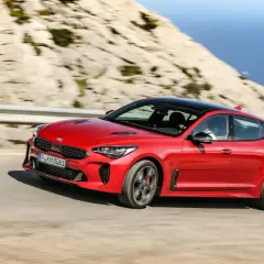 Czerwony Kia Stinger GT pędzi po krętej drodze z widokiem na morze.
