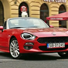 Czerwony Fiat 124 Spider z otwartym dachem sunie ulicą przed kawiarnią Costa Coffee.