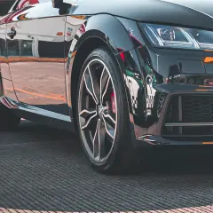 Zbliżenie na czarne, sportowe auto z widoczną felgą i oponą.