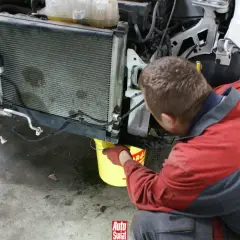 Mechanik w rękawiczkach nalewa środek do uszczelniania chłodnic do żółtego wiadra pod samochodem.