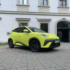 Jaskrawożółty BYD Seagull zaparkowany na bruku przed budynkiem z łukowym wejściem.