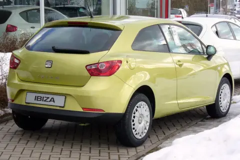 Jasnożółty Seat Ibiza 1.4 benzyna z tyłu, zaparkowany na kostce brukowej, obok śniegu.