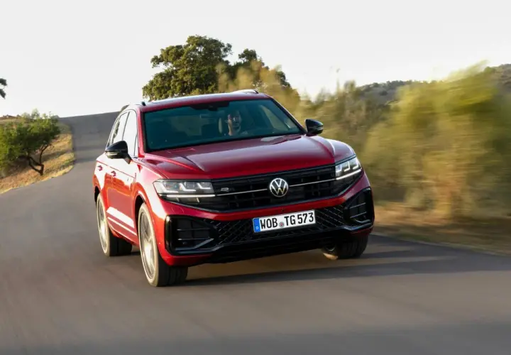 Czerwony Volkswagen Touareg 2024 pędzi po krętej drodze wśród wzgórz.