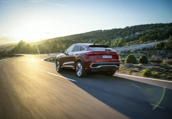 Czerwony samochód Audi coupe na krętej drodze w górach o zachodzie słońca.