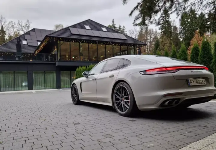 Białe Porsche Panamera GTS przed nowoczesnym budynkiem z panelami słonecznymi. Idealny wybór dla firm ceniących leasing operacyjny.
