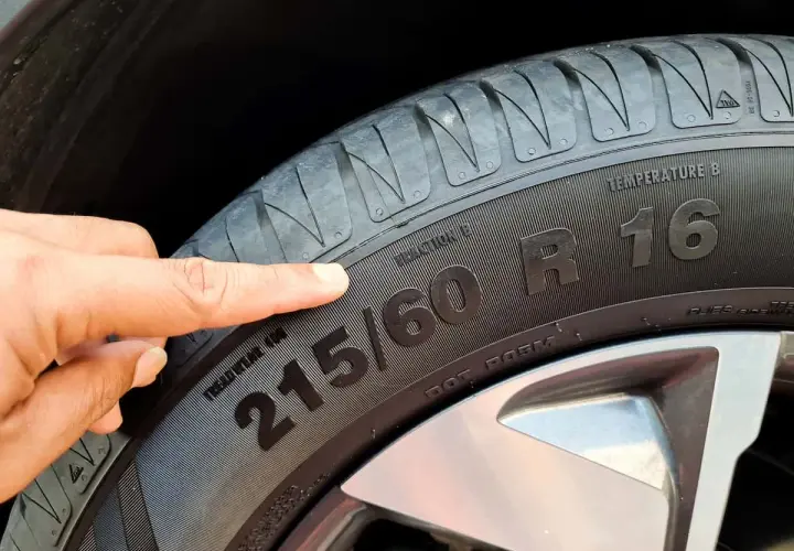 Palec wskazuje na oznaczenie opon 215/60 R16, informujące o rozmiarze i typie.