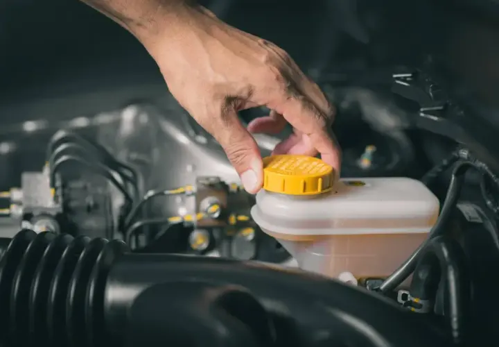 Dłoń odkręca żółtą zakrętkę zbiornika płynu hamulcowego. To właśnie tam znajduje się zbiornik płynu hamulcowego BMW E39.