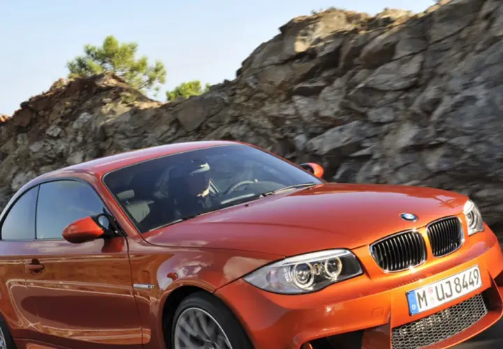 Pomarańczowy bmw1 z kierowcą za kierownicą pędzi po górskiej drodze.
