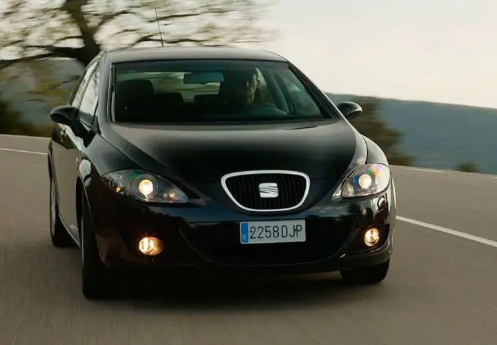Czarny Seat Leon 2 jedzie po krętej drodze wśród drzew.