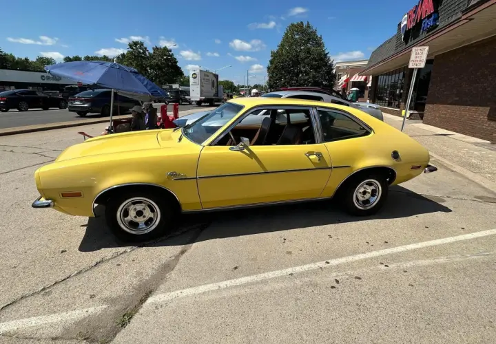 Żółty Ford Pinto z lat 70. stoi zaparkowany przy ulicy, obok sklepu.