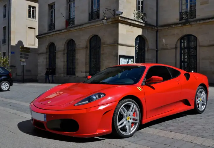 Czerwone Ferrari F430 zaparkowane na brukowanej ulicy przed kamienną kamienicą.