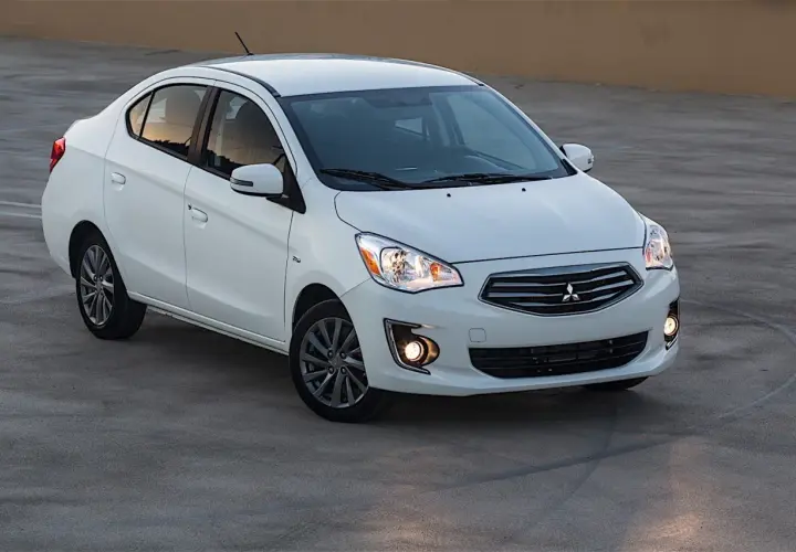 Biały sedan Mitsubishi Mirage zaparkowany na betonowej nawierzchni.