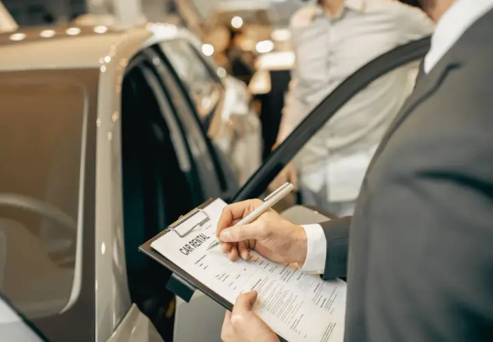 Mężczyzna w garniturze podpisuje dokument "CAR RENTAL" przy luksusowym samochodzie.