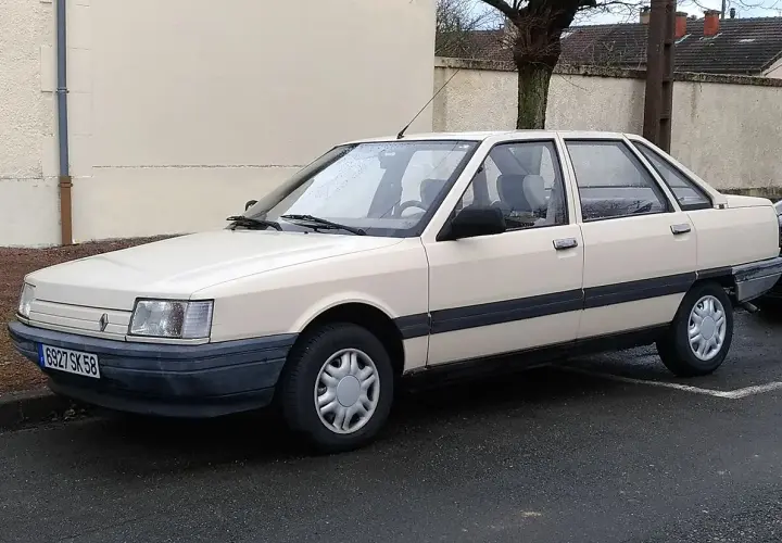 Jasny beżowy sedan Renault 21 z lat 80. stoi na mokrej drodze.