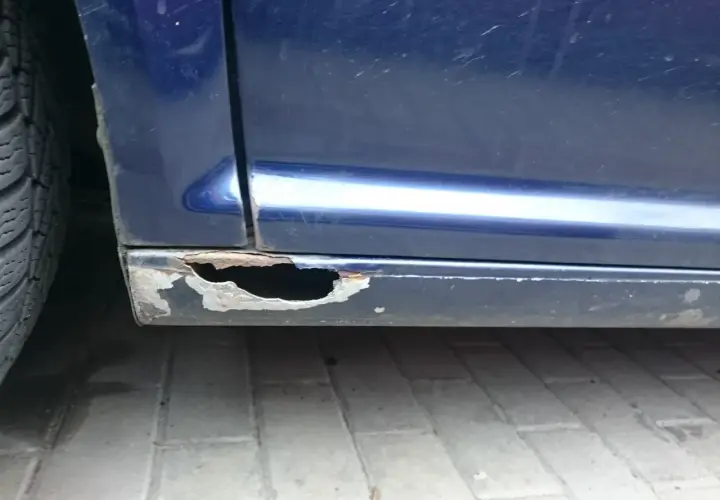 Widoczne są poważne dziury w progach niebieskiego samochodu, co pokazuje, jak załatać dziury w samochodzie.