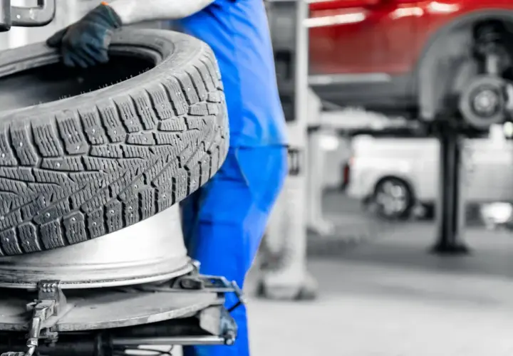 Mechanik w niebieskim kombinezonie wymienia oponę. Dowiedz się, ile kosztuje wymiana opon w Twojej okolicy.